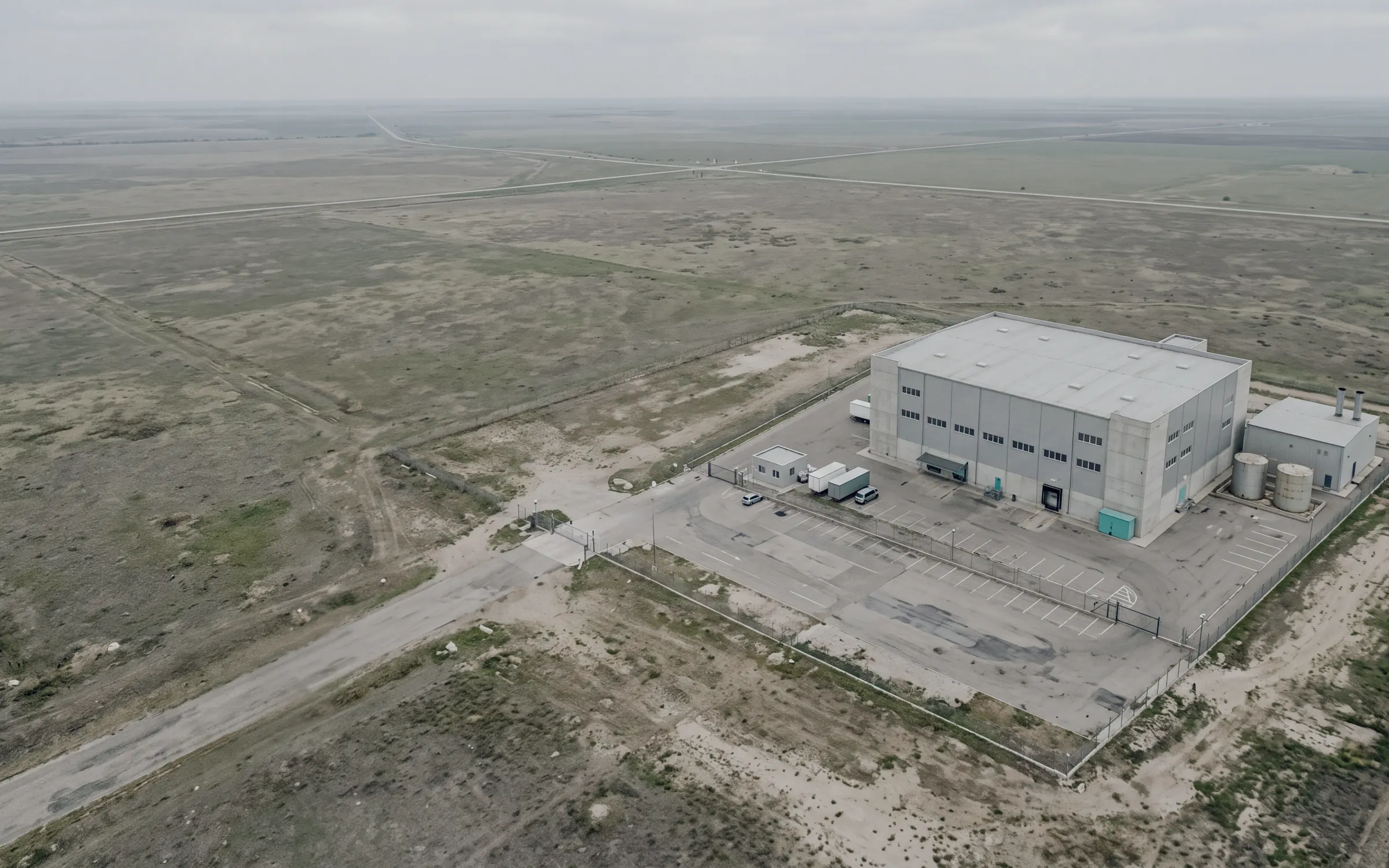 AI-generated scene: a logistics park with its long warehouse, tanks and fenced yard, seen from the air.